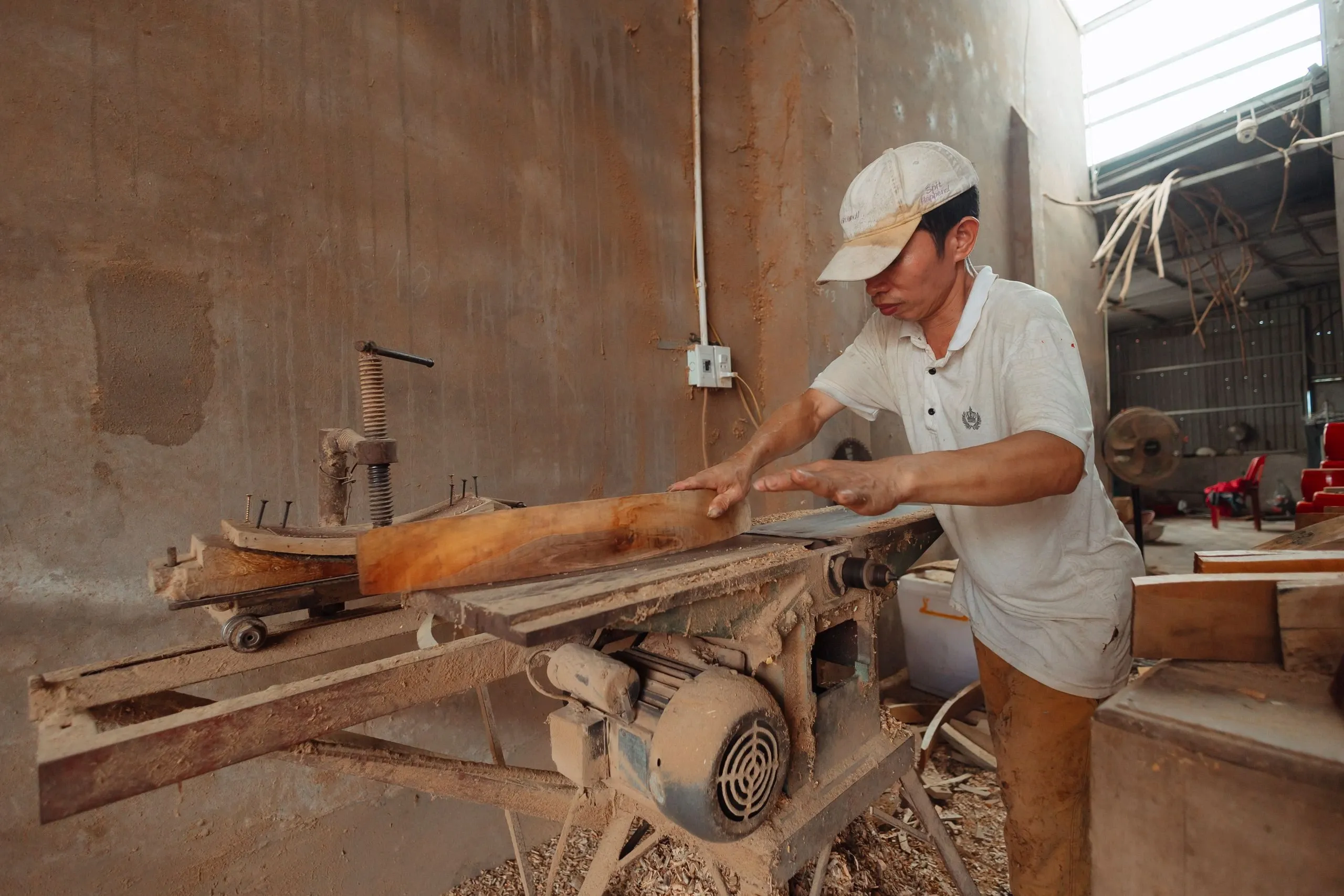 Un menuisier dégrossit une grosse pièce de bois sur une machine, dans un atelier poussiéreux