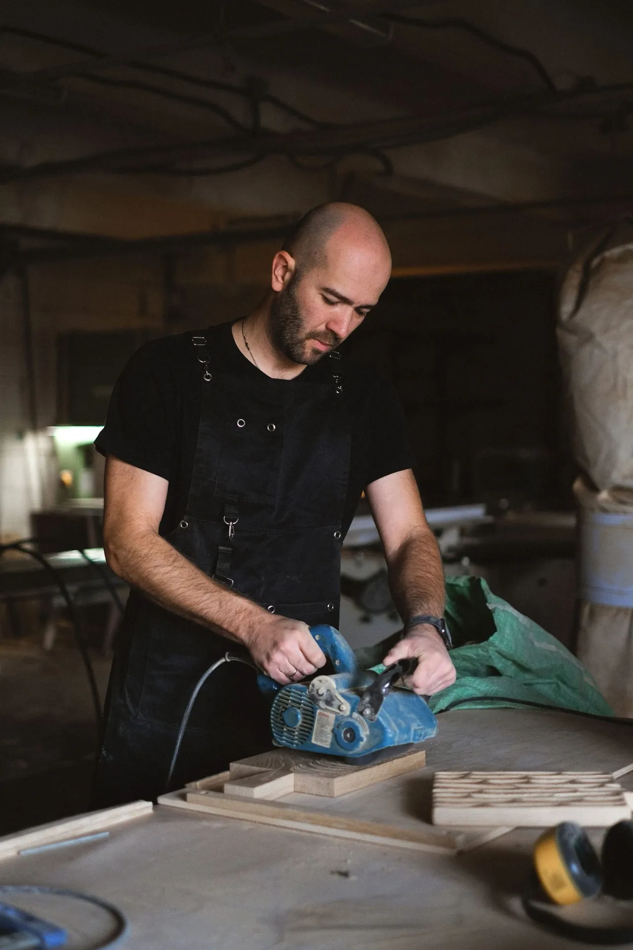 Antoine, en tablier noir, ponce une pièce sur l'établi de l'atelier
