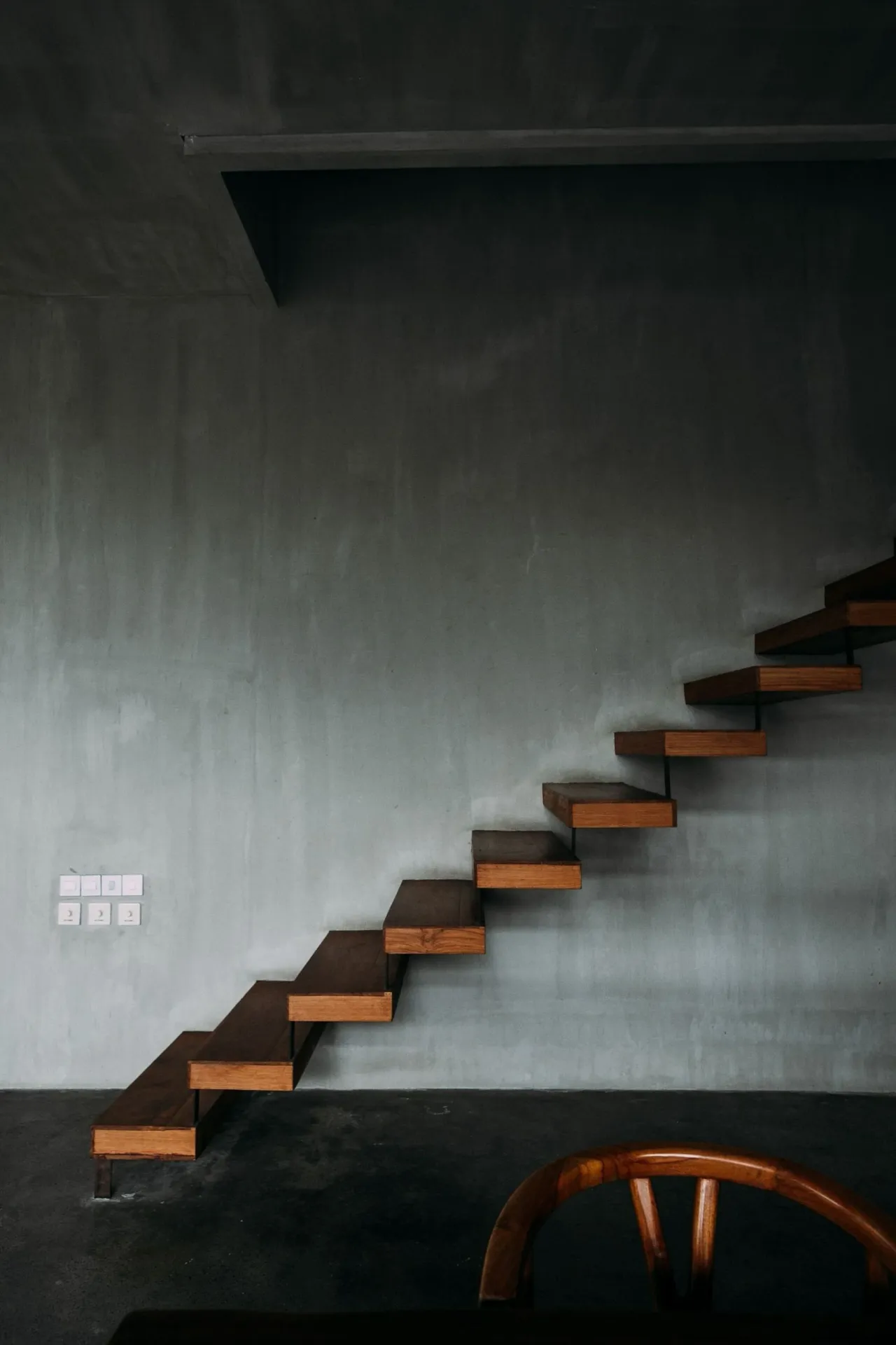 Un escalier aux marches de bois fixées dans un mur gris, sans contremarches