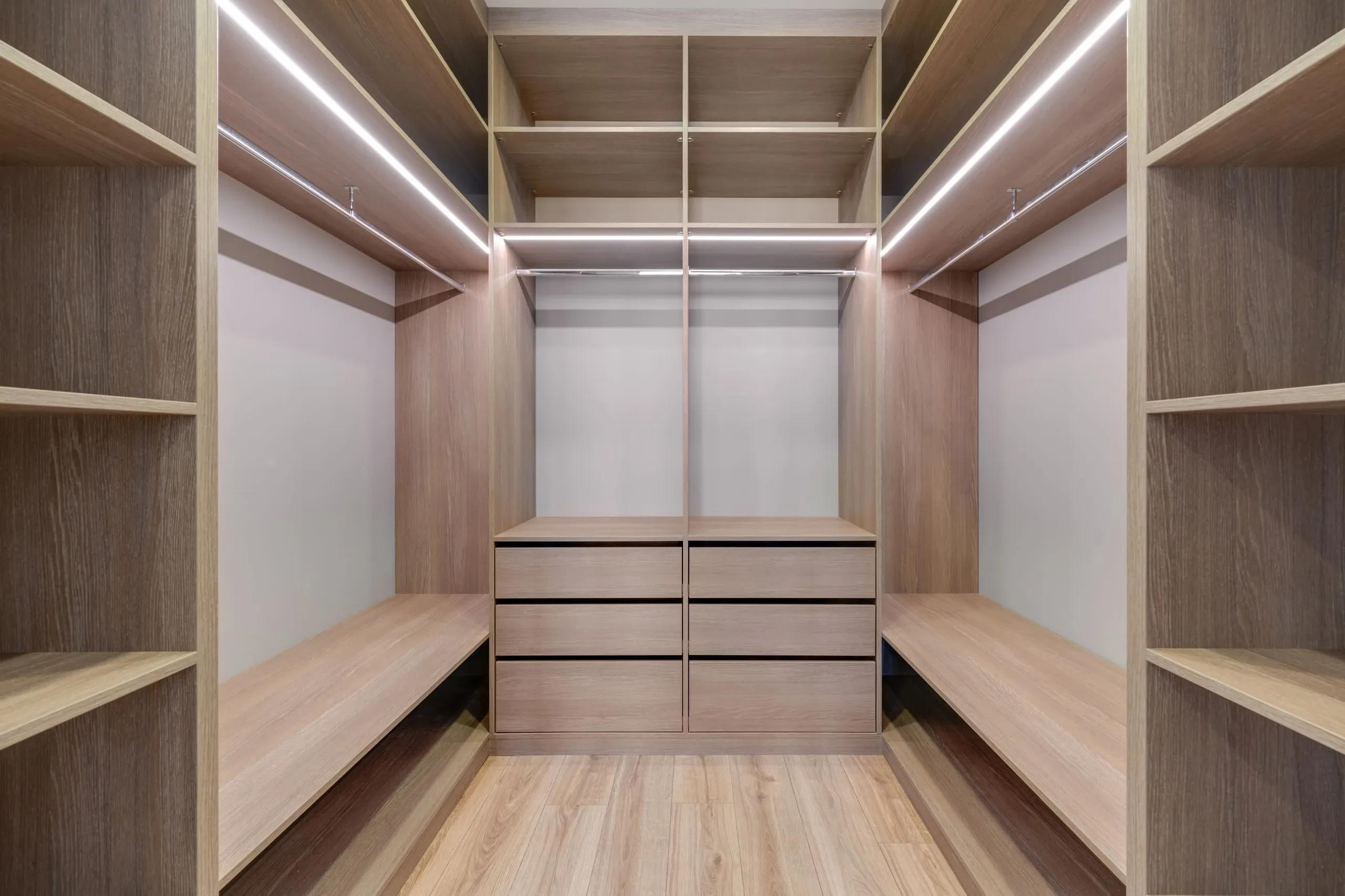 Un dressing en bois clair, avec étagères, penderies éclairées et tiroirs